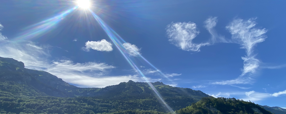 Sonnenstrahlen über grünen Bergen unter blauem Himmel